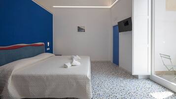 A modern hotel room with a bed, a small bedside table, a TV mounted on the wall, and a glass door leading to a balcony.