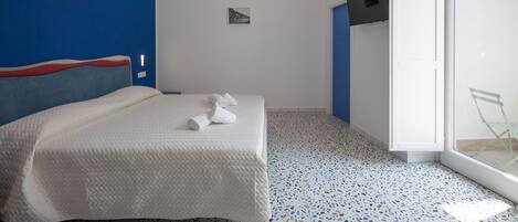 A modern hotel room with a bed, a small bedside table, a TV mounted on the wall, and a glass door leading to a balcony.