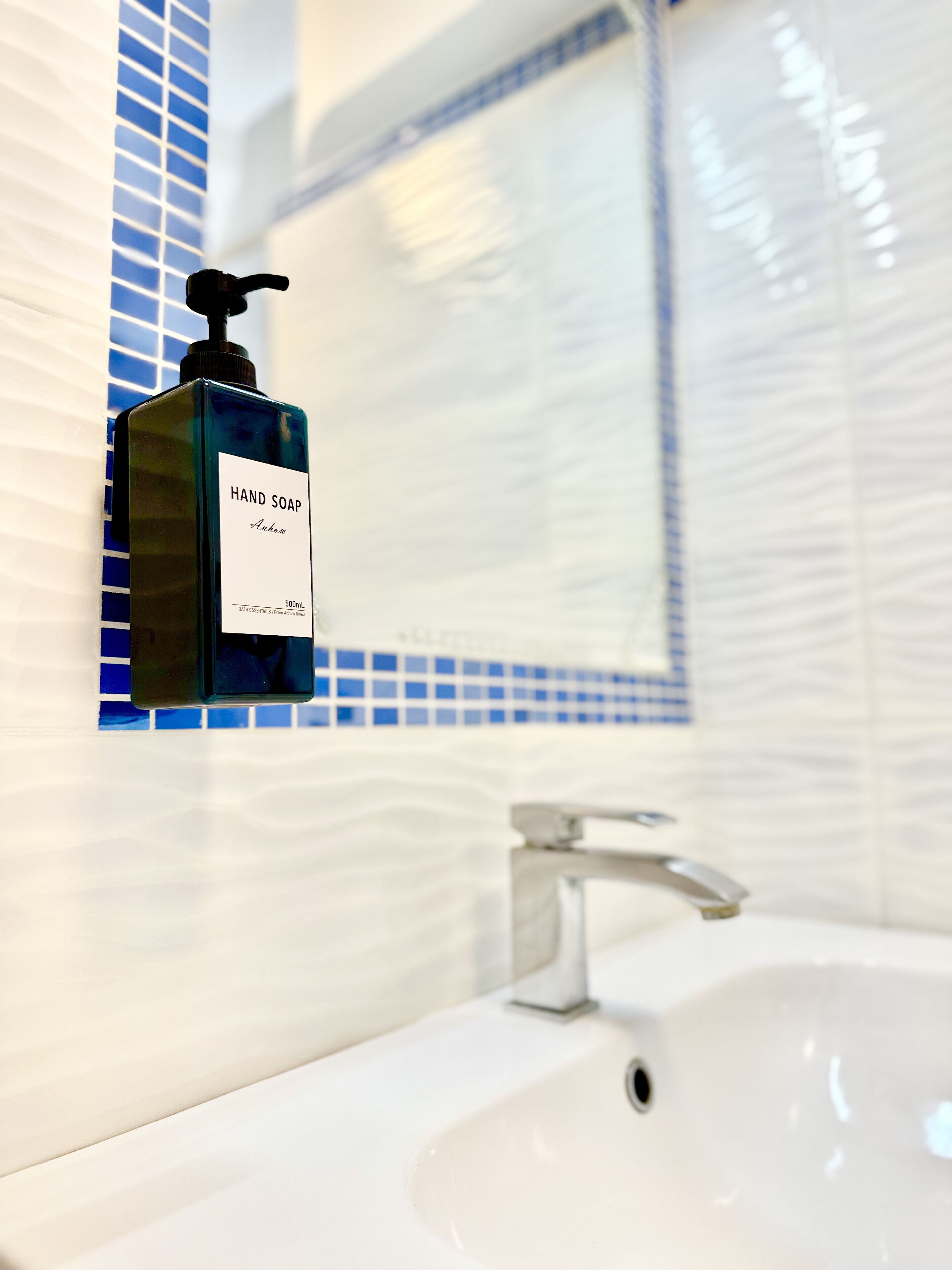 A bathroom with a white sink, a mirror, and a bottle of hand soap.