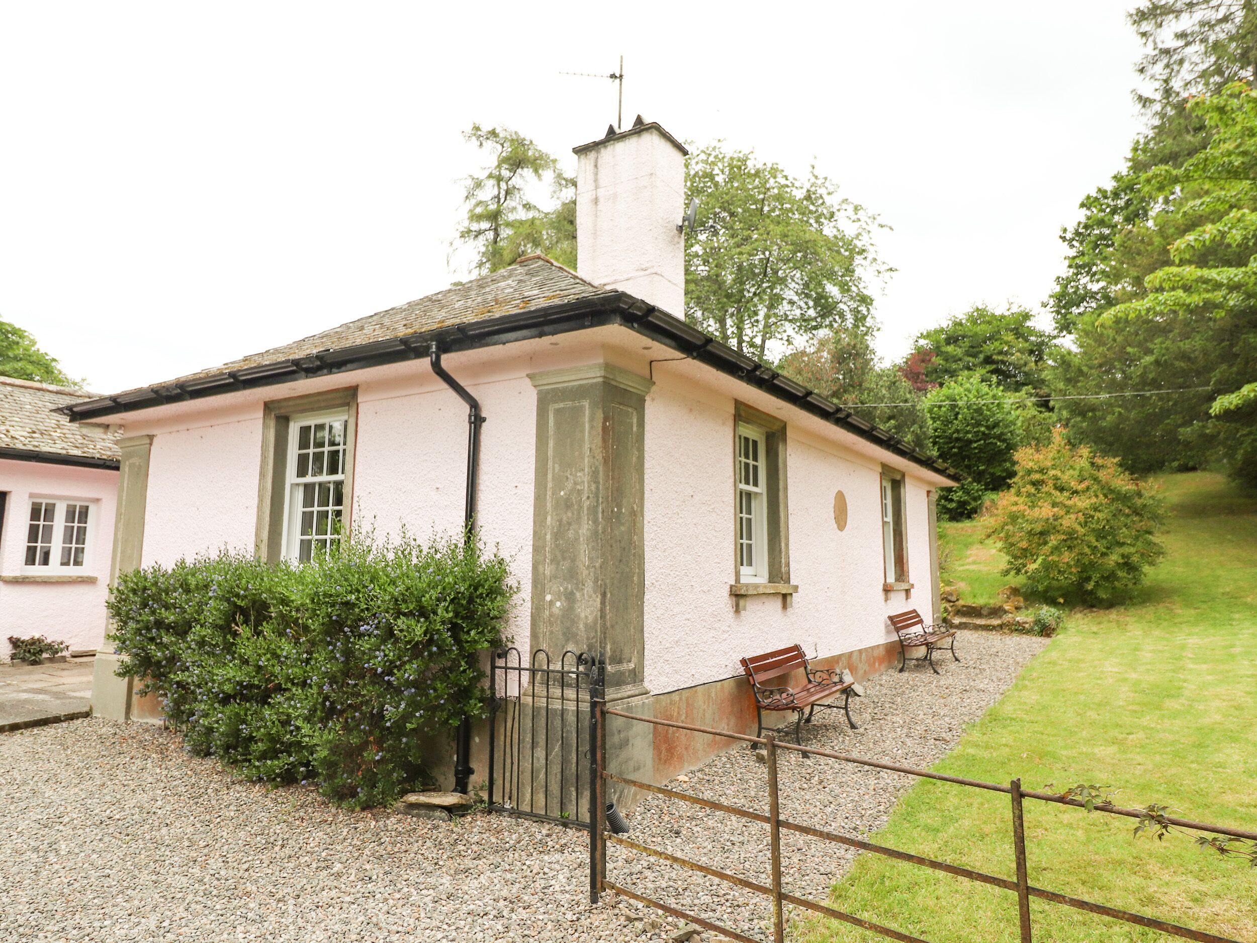 A small, single-story building with a white exterior and a black roof. It has a chimney, a window with a white frame, and a small porch area with a bench.