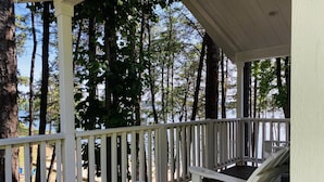 A wooden deck with a white railing, a covered area, and a view of trees and a body of water. - Beach-view Studio Cabin with Private Porch - #13 (Charlotte)