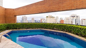 Una piscina en la azotea con vista a la ciudad, rodeada por un muro de ladrillo y setos verdes.