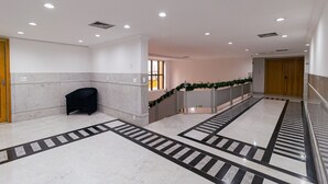 Un vestíbulo de hotel con piso de mármol, un banco negro y una puerta de madera.