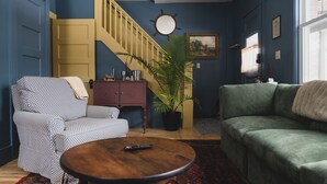 Una sala de estar con un sofá, un sillón, una mesa de centro y una escalera con barandilla amarilla.