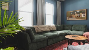 Una sala de estar con un sofá verde, una mesa de centro redonda de madera y un tapete rojo estampado.