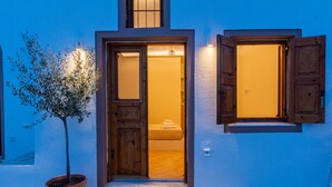 A building with a wooden door and window, a potted plant, and a tiled floor. - Ostria Caldera Studio 2 (Thira - Santorini)