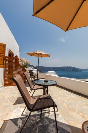 Um terraço com mesa redonda e duas cadeiras, um grande guarda-sol e vista para o mar.