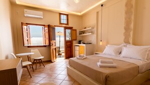 A hotel room with a bed, a desk, chairs, a kitchenette, and a bathroom. - Ostria Caldera Studio 2 (Thira - Santorini)