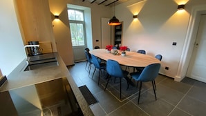 A modern kitchen with a large island, a dining area with a wooden table and blue chairs, and a window with natural light.
