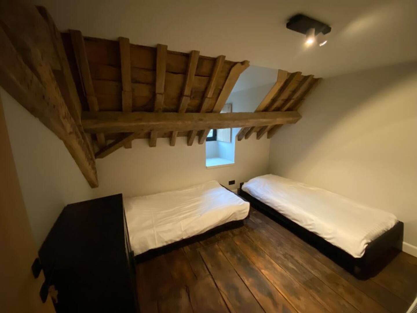 Ein kleiner, rustikaler Raum mit Holzbalken, zwei Einzelbetten und einem kleinen Fenster.