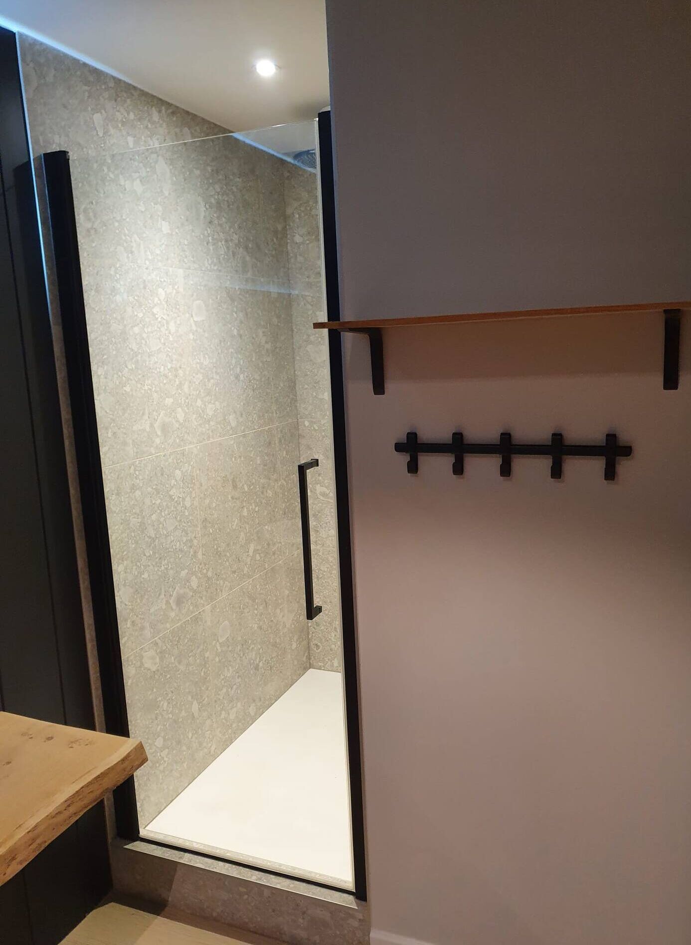A modern bathroom with a shower area, a wooden bench, and a wall-mounted rack.