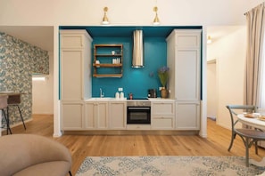 Cocina compacta con armarios blancos, una pared de acento color turquesa, horno empotrado e iluminación colgante.