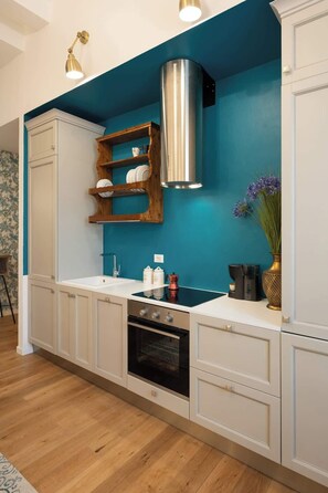 Une cuisine avec des meubles blancs, un mur d’accent de couleur turquoise, une hotte de cuisinière en acier inoxydable et une étagère en bois où sont disposés de la vaisselle.
