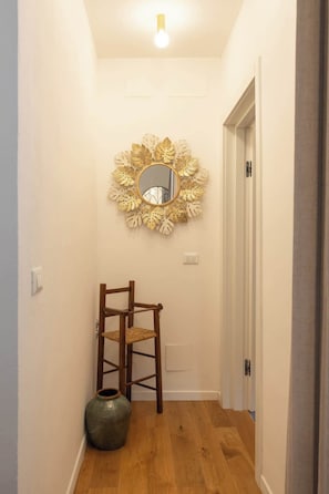Un pasillo con una silla de madera, un jarrón grande y un espejo con motivos de hojas.