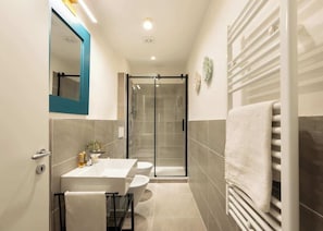 A modern bathroom with a glass shower enclosure, a white sink, and a towel rack.