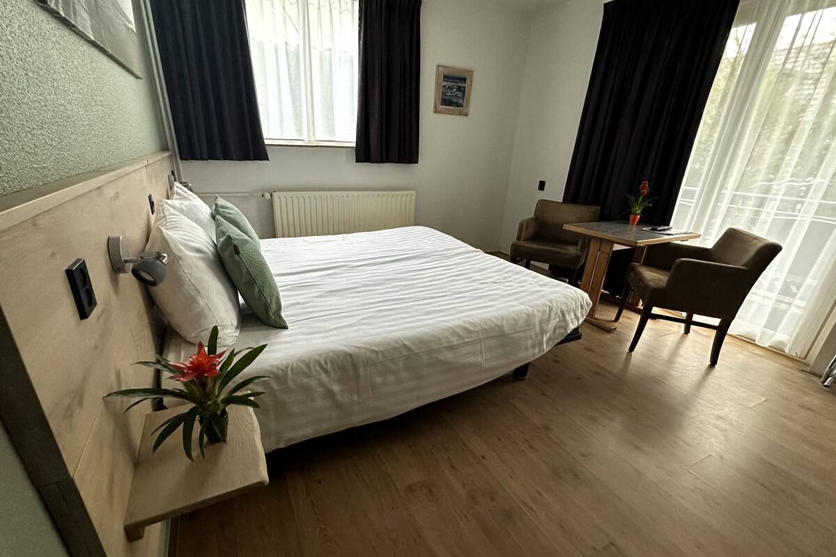 Ein Hotelzimmer mit Bett, Stuhl, einem kleinen Tisch und einer Topfpflanze.