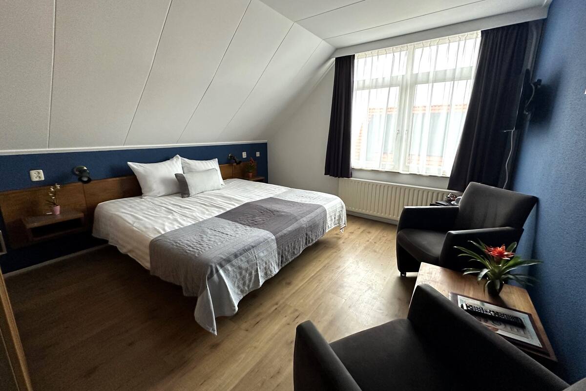 Ein Hotelzimmer mit einem großen Bett, einem Schreibtisch mit Stuhl, einem Fenster mit Vorhängen und einem Heizkörper.