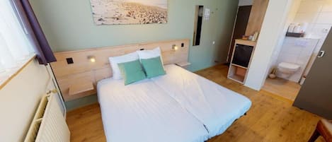 A bedroom with a large bed, a headboard with lights, a painting on the wall, and a bathroom visible through an open door.