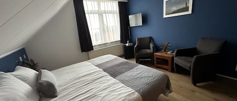 Ett hotellrum med en stor säng, en stol, ett litet bord och ett fönster med gardiner.