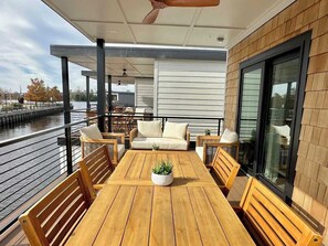 Ein überdachter Außenbereich mit Holztisch und -stühlen, einer Couch und einem Blumentopf.