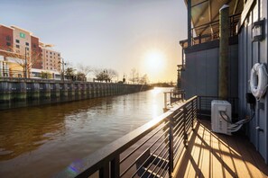 A waterfront hotel with a view of the river, a wooden deck, and a building with a visible 'E' sign. - Surfside at The Cove Riverwalk Villas (Wilmington)