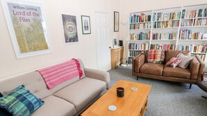 A living room with a beige sofa, a brown leather couch, a wooden coffee table, and a bookshelf filled with books. - The Bookshelf (Swansea)