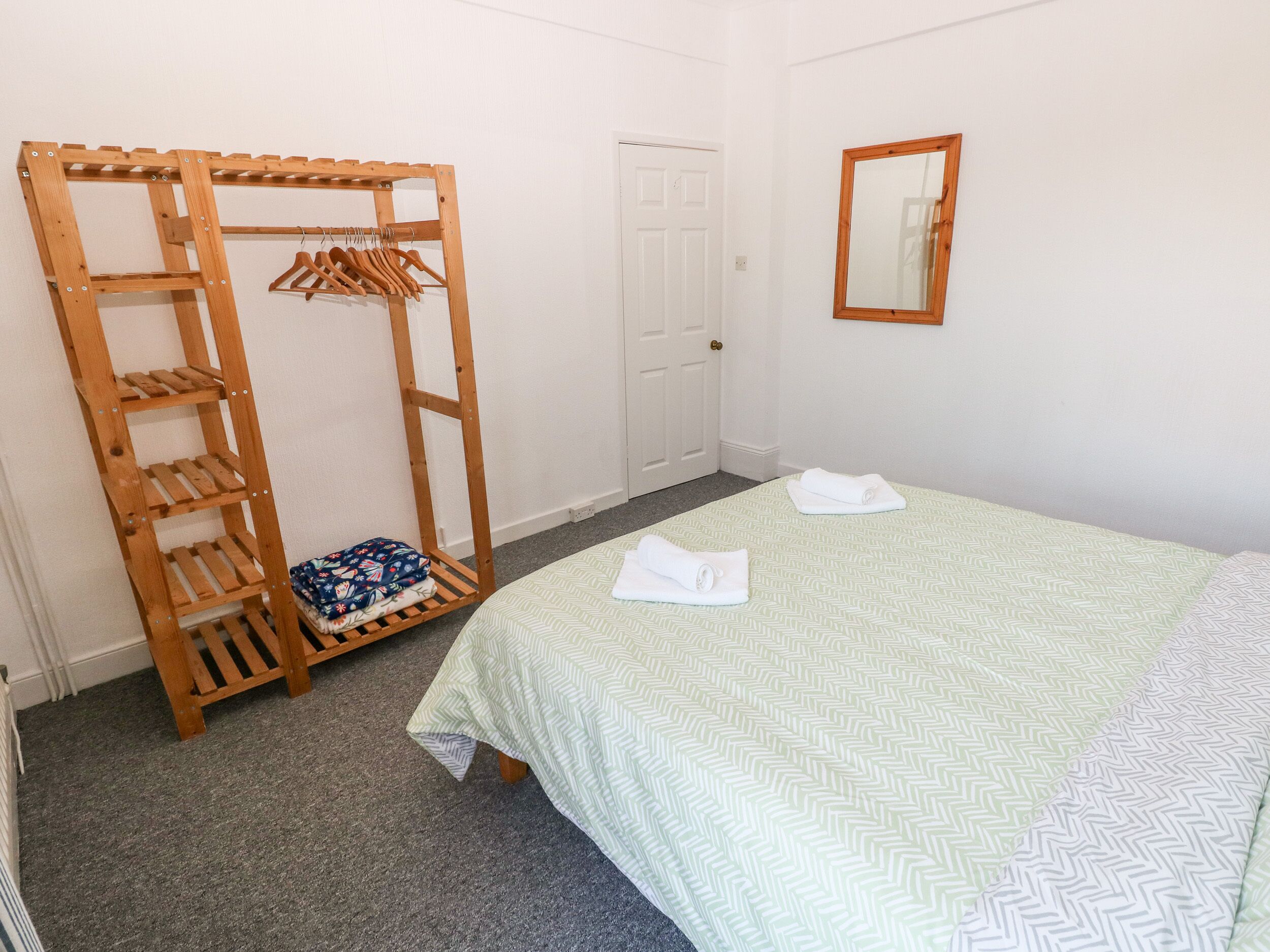 A bedroom with a bed, a wooden wardrobe, a door, and a mirror on the wall.