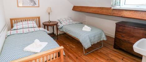 A cozy room with two wooden beds, a small table with a lamp, a dresser, and a window with curtains.