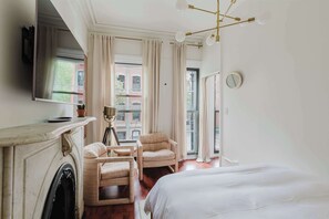Hotelkamer met een open haard, een bed, een zithoek met twee stoelen, een aan de muur bevestigde televisie en een groot raam met gordijnen.