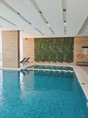 A swimming pool with clear blue water, a tiled deck, and a wall with a green leafy pattern. - A Luxurious Sea View 1 Bedroom Apartment (Al HIDD)