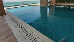 A modern indoor swimming pool with a view of the ocean, featuring a wooden deck and a glass wall. - A Luxurious Sea View 1 Bedroom Apartment (Al HIDD)