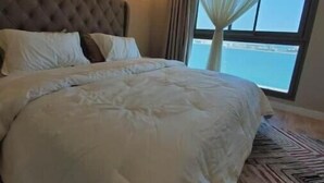 A large bed with a tufted headboard, white bedding, and a patterned rug. - A Luxurious Sea View 1 Bedroom Apartment (Al HIDD)