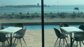 Une pièce dotée de grandes fenêtres donnant sur une plage et l’océan, avec un plancher en bois et un mobilier moderne.