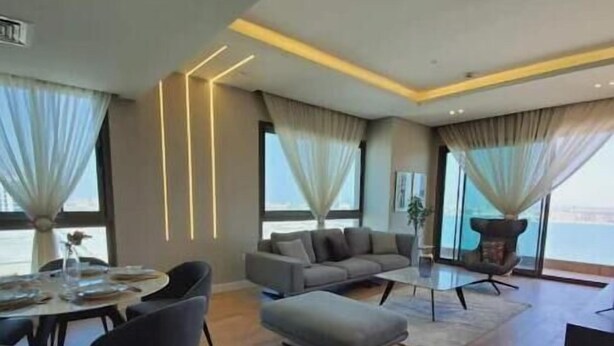 Un salon moderne avec un canapé gris, une table à manger avec des chaises et une grande fenêtre avec des rideaux.