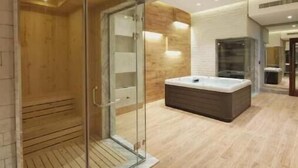 Une salle de spa moderne dotée d’un sauna à parois de verre, d’un plancher en bois et d’une grande table de massage.