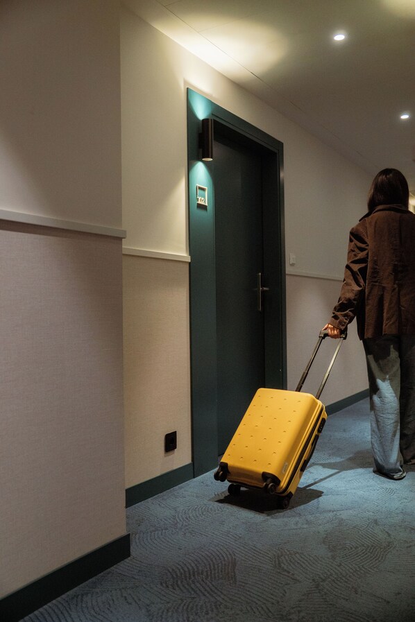 A person pulling a yellow suitcase down a carpeted hallway with a door at the end. - BYPILLOW Bilbo (Bilbao)