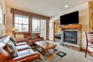 A living room with a fireplace, leather sofa, and a flat-screen TV. - Ski-In/Ski-Out Granby Ranch Condo w/ Pool Access (Granby)