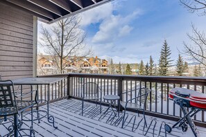 A covered outdoor deck with metal chairs and a grill, overlooking a snowy residential area.