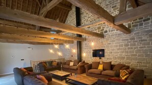 A spacious living room with a high ceiling, exposed wooden beams, and a stone wall. There are multiple sofas and a coffee table arranged for seating. - La Tannerie De Durbuy - 28 Personen (Durbuy)