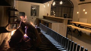 A cozy interior with a fireplace, wooden benches, and hanging light bulbs. - La Tannerie De Durbuy - 28 Personen (Durbuy)