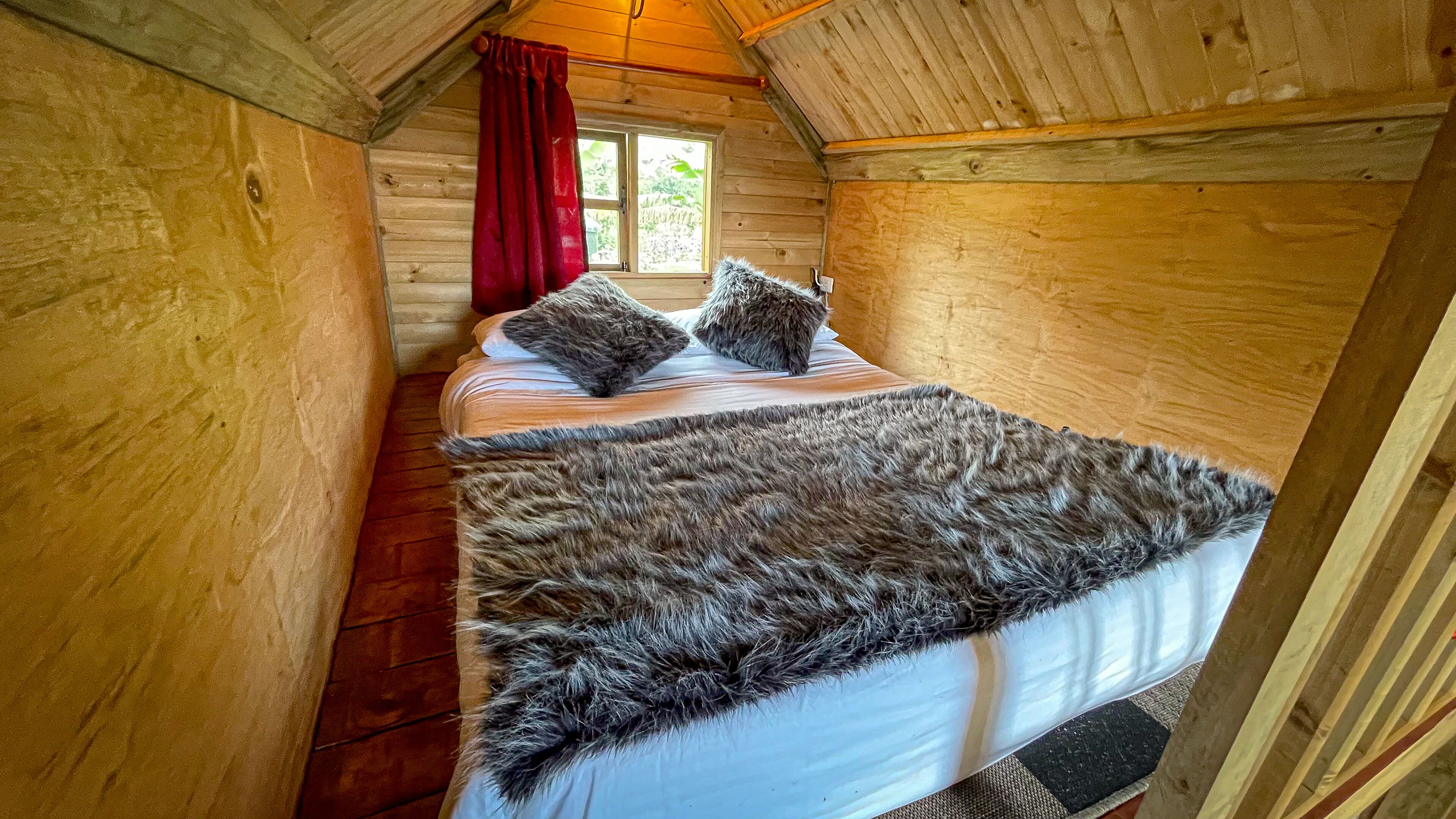 Dormitorio de cabaña de madera con cama, almohadas y cortina roja.