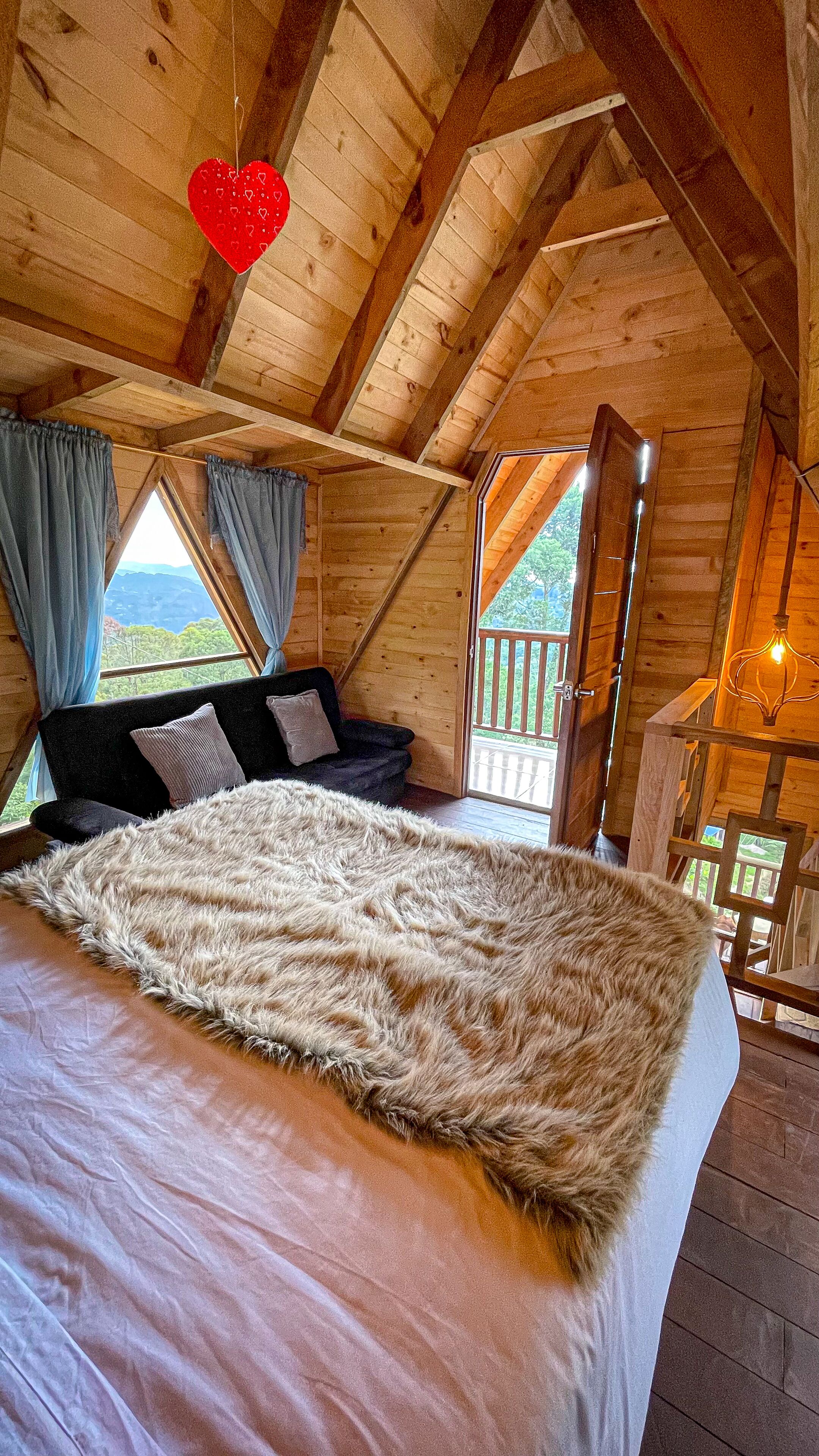 A cozy bedroom with a large bed, a wooden ceiling, and a view of the outdoors through a window.
