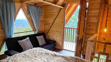 A cozy bedroom with a large bed, a wooden ceiling, and a view of the outdoors through a window.