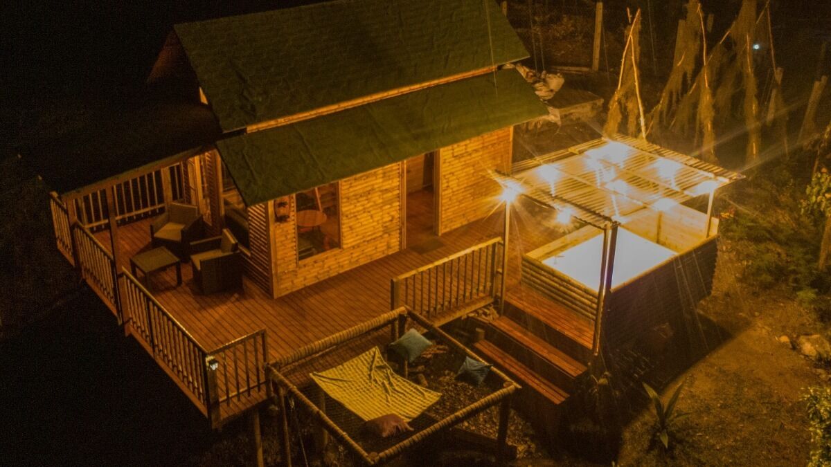 Une cabane en bois dotée d’une terrasse, d’un petit espace extérieur aménagé pour s’asseoir et d’une véranda en verre.