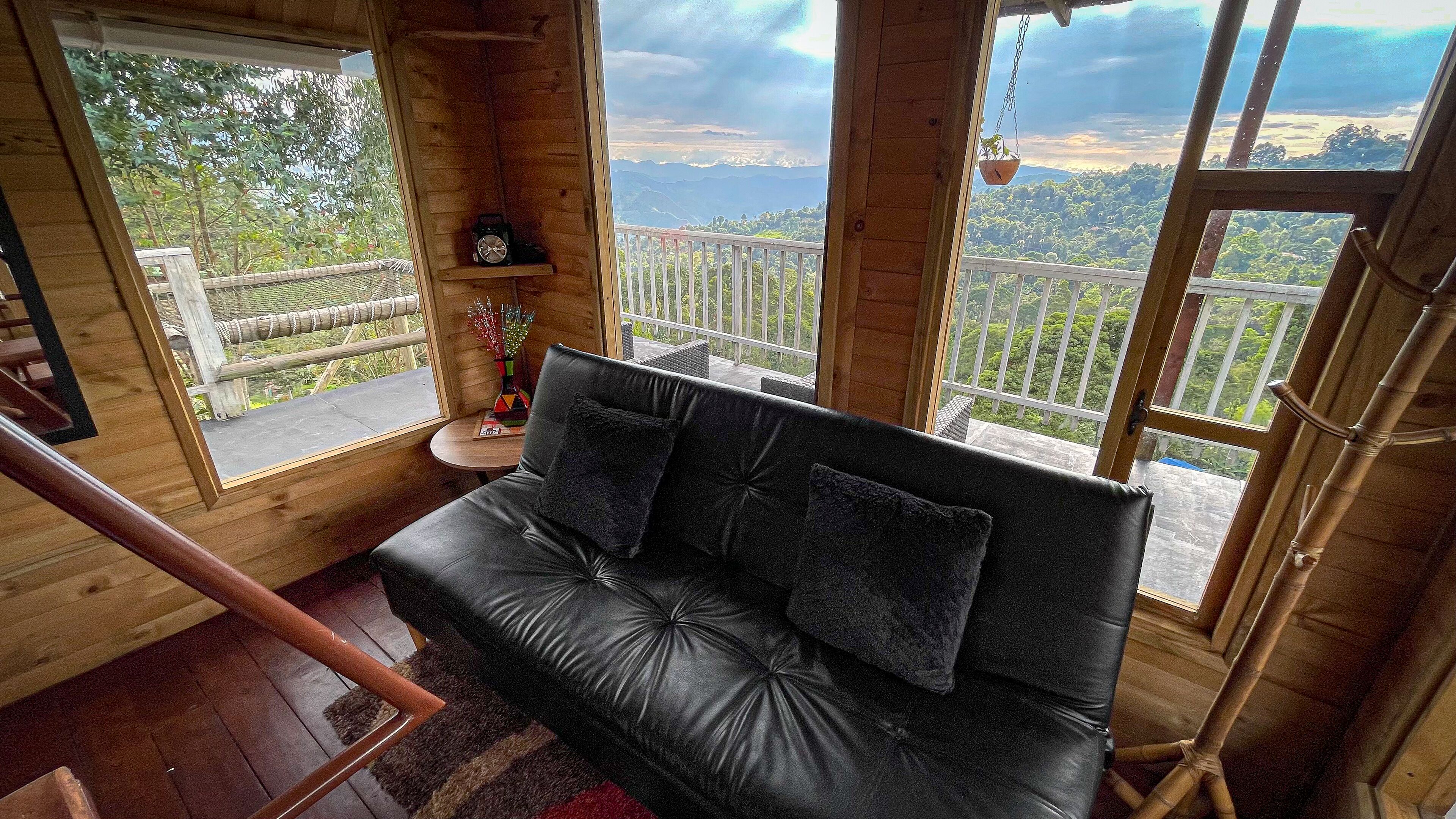 Habitación de cabaña de madera con un sofá de cuero negro, una mesita con un florero y vistas a la montaña a través de amplios ventanales.