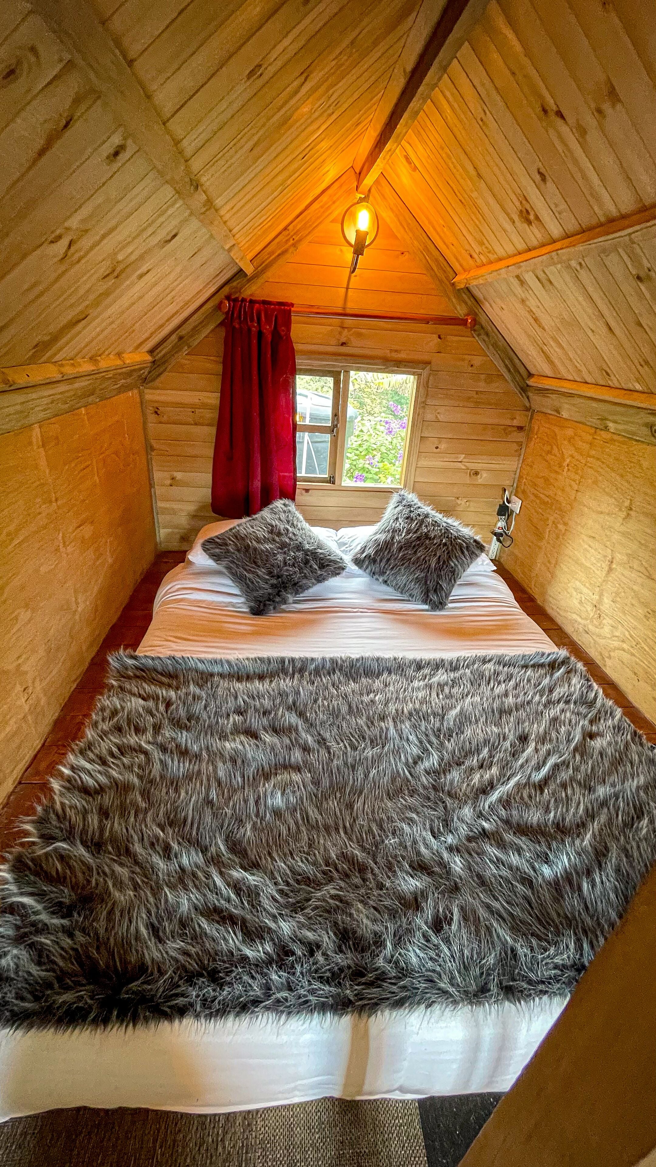Une chambre confortable située dans les combles, avec un plafond en bois, une grande couverture en fourrure sur le lit et une fenêtre donnant sur un paysage verdoyant.