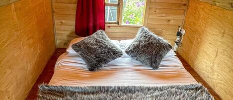 Une chambre confortable située dans les combles, avec un plafond en bois, une grande couverture en fourrure sur le lit et une fenêtre donnant sur un paysage verdoyant.
