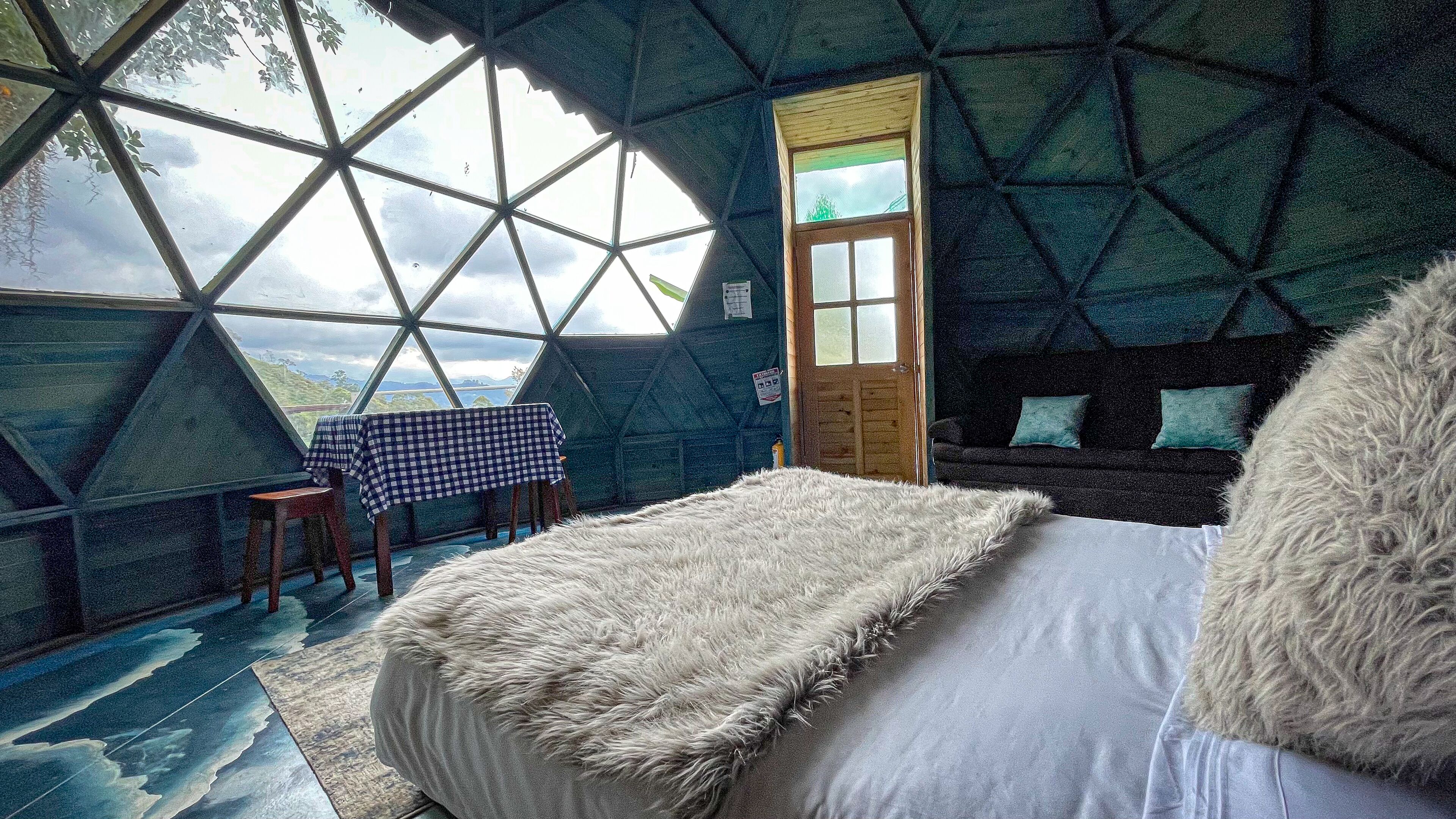 Una habitación acogedora con una mesa a cuadros, una cama mullida y vistas al exterior a través de un amplio ventanal.