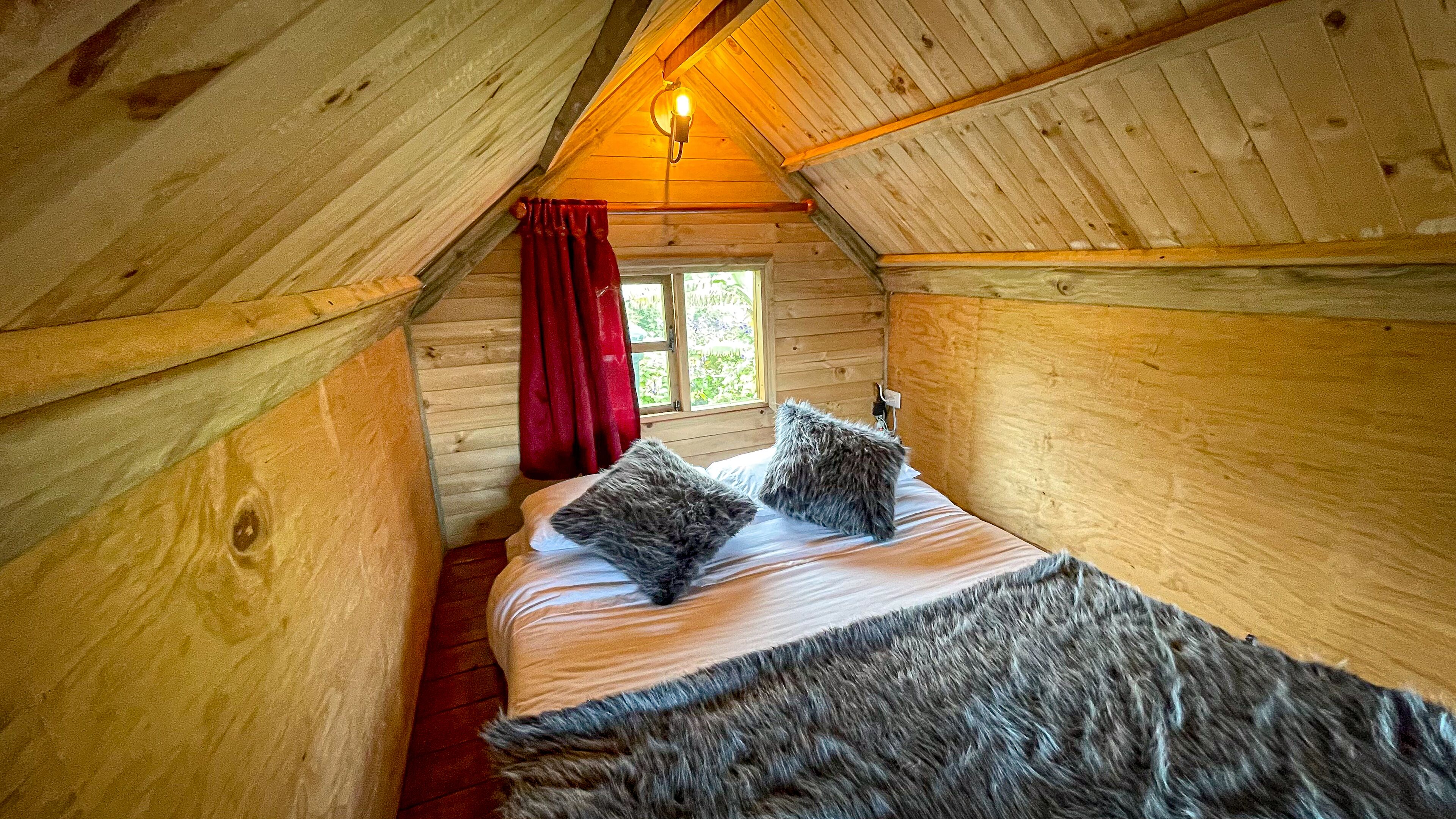 A cozy wooden cabin room with a bed, a window, and a red curtain.