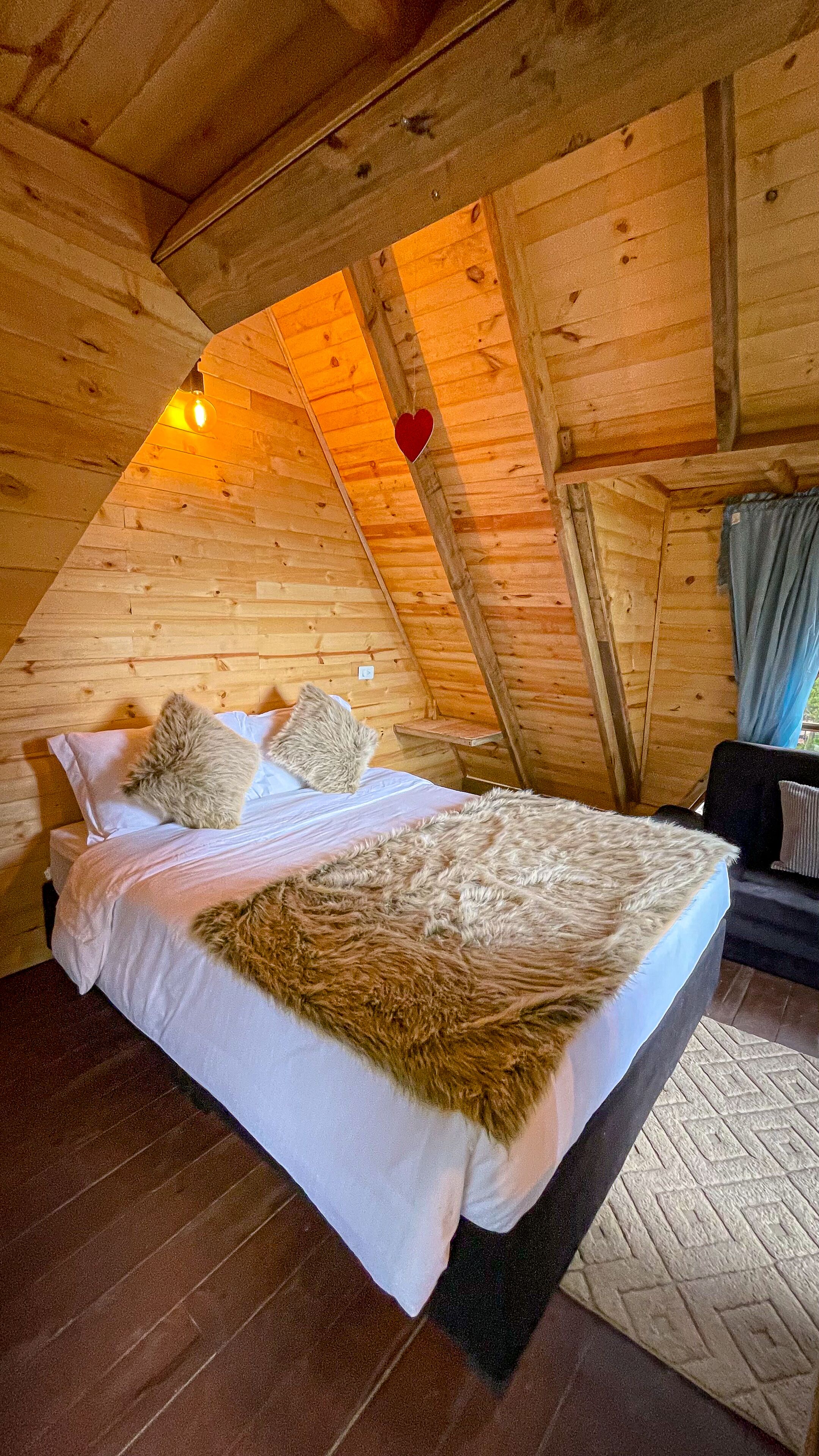 Ein gemütlicher Holzraum mit einem Bett, Kissen und einer herzförmigen Dekoration an der Decke.